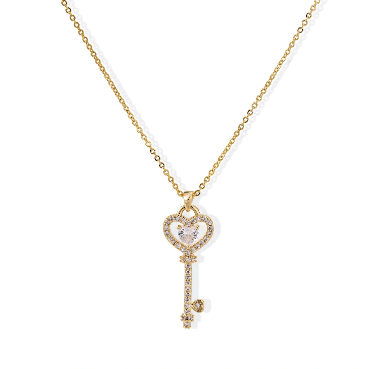 Delicate gold key pendant with heart-shaped bow and crystal pavé detailing on fine chain against cream background.