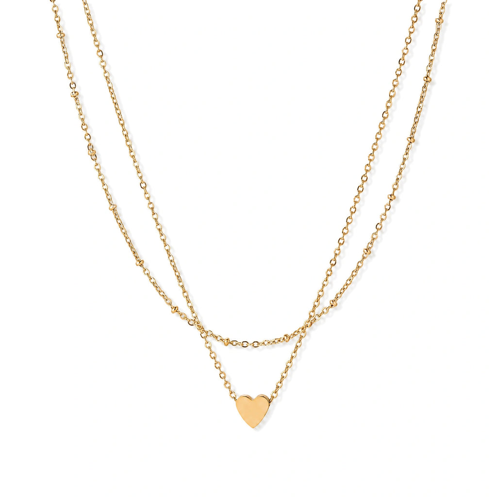 Delicate double-chain gold necklace with tiny heart pendant on cream background