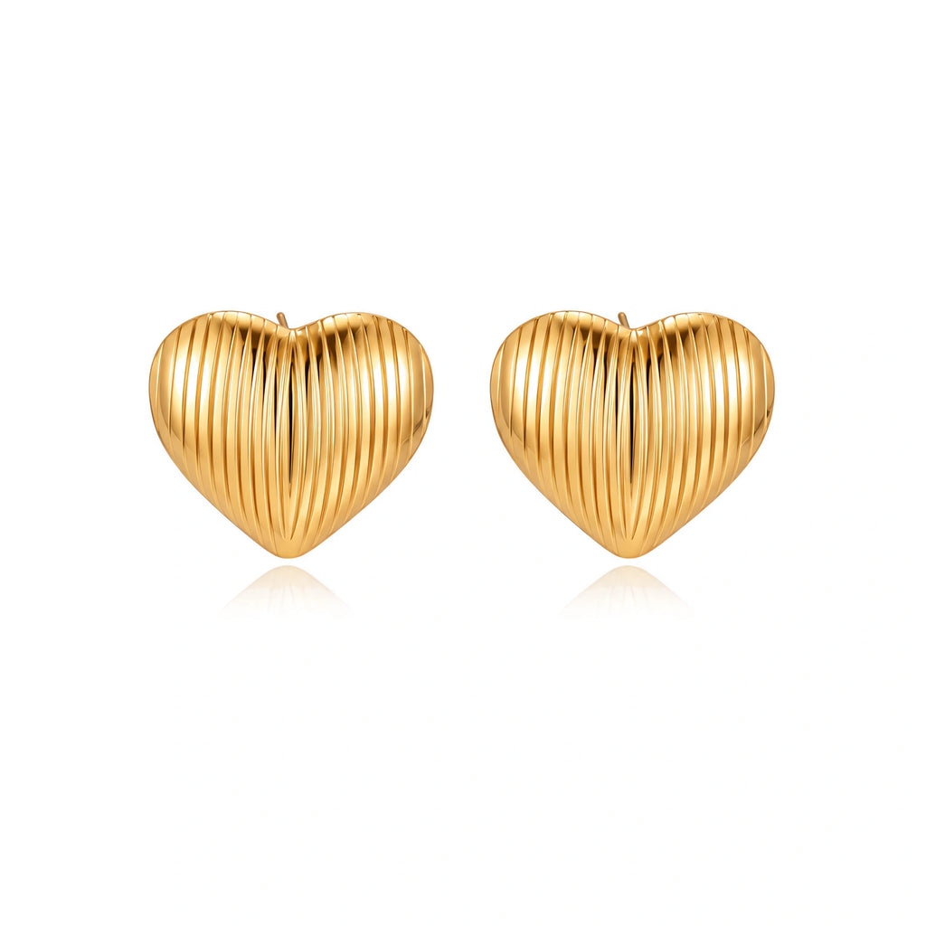Gold heart-shaped stud earrings with parallel ridged texture on cream background