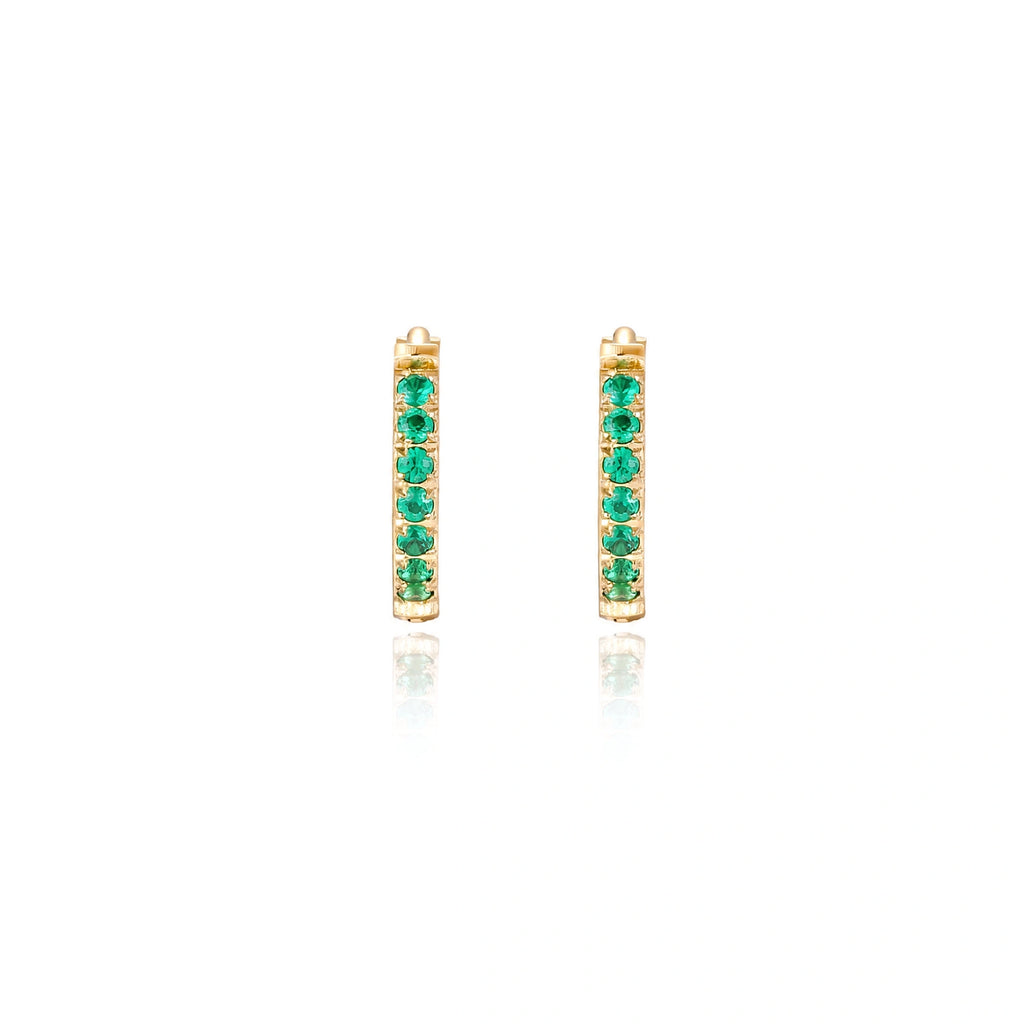Pair of small gold huggie hoop earrings with bright green cubic zirconia stones on cream background