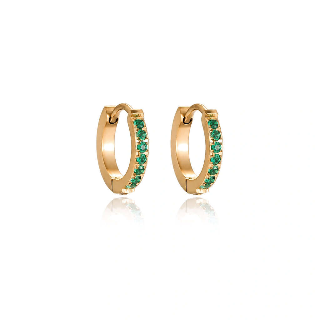Pair of small gold huggie hoop earrings with bright green cubic zirconia stones on cream background