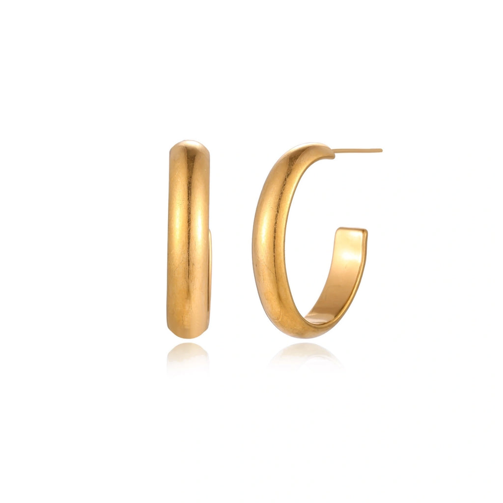 Chunky tubular hoop earrings in warm 14K gold-plated finish with smooth polished surface on cream background.