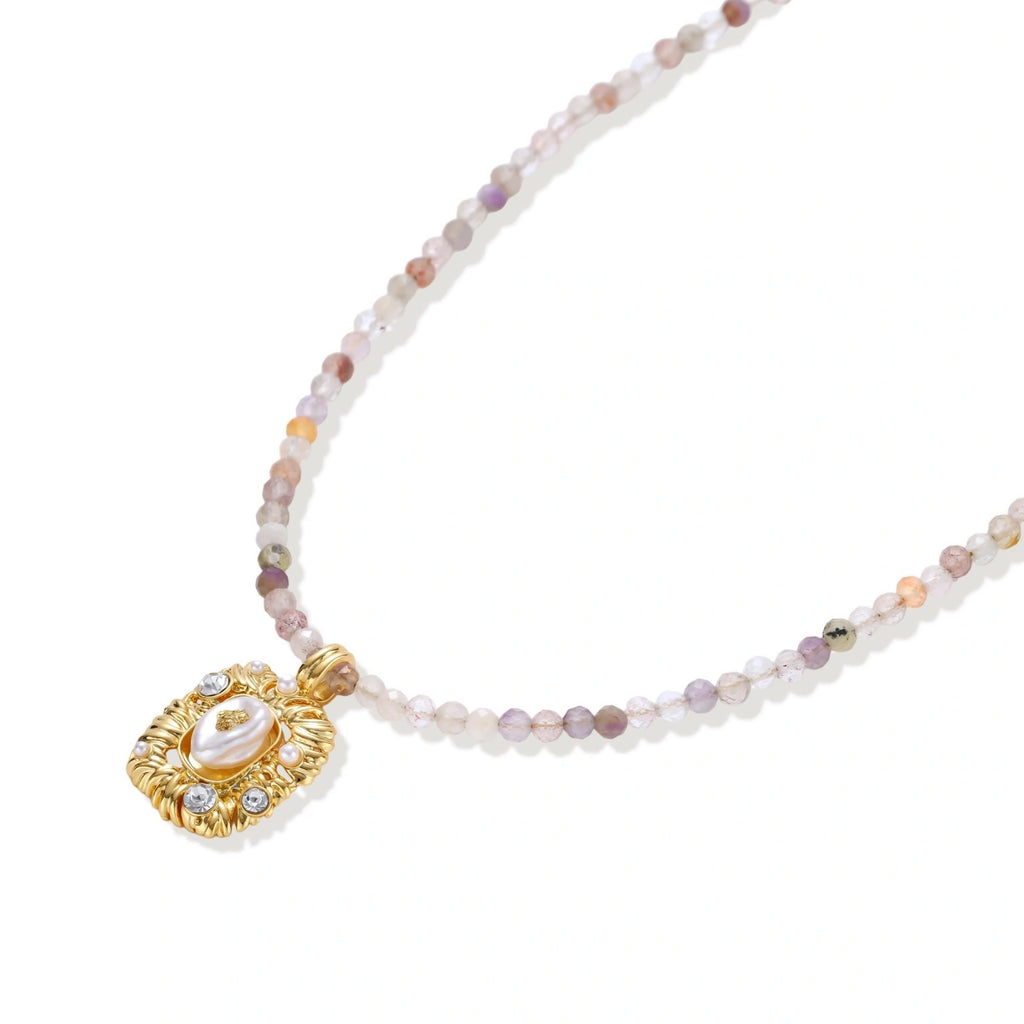 Ornate gold-plated pendant necklace with multicolored gemstone beads in purple, pink and clear tones on white background
