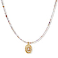 Delicate gold-plated necklace with mixed gemstone beads and ornate oval pendant on white background